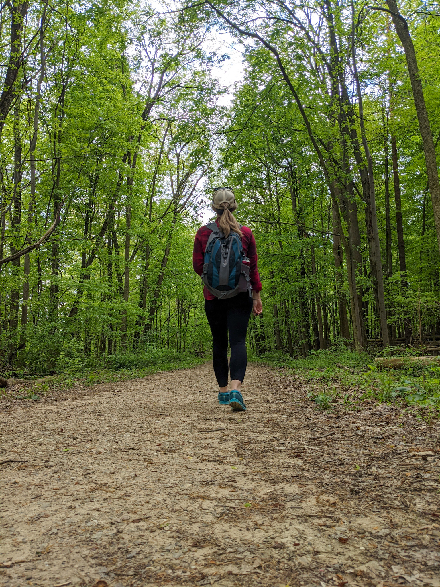 Caucasian woman walks away from the camera on a hiking trail surrounded by green trees